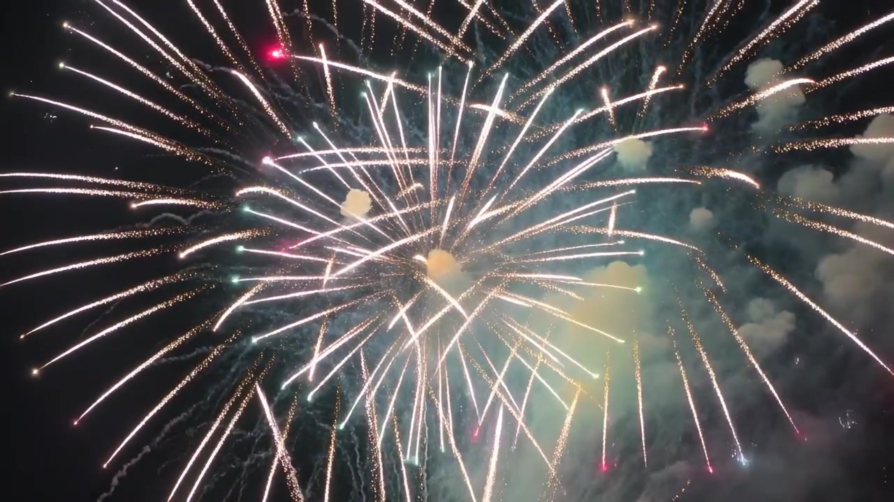 Fuochi d'artificio aerei che si accendono creando esplosioni rotonde nel cielo notturno con scie a cometa, scintille, fumo