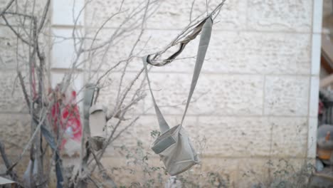 bag hanging from dead tree in gaza, near a wall with rubble in background, symbol of abandonment and conflict - palestine