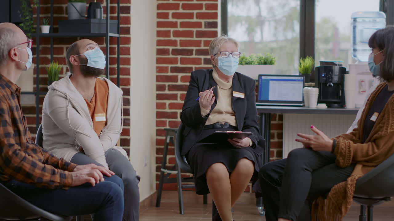 Woman therapist giving advice to people at aa group meeting, wearing face mask