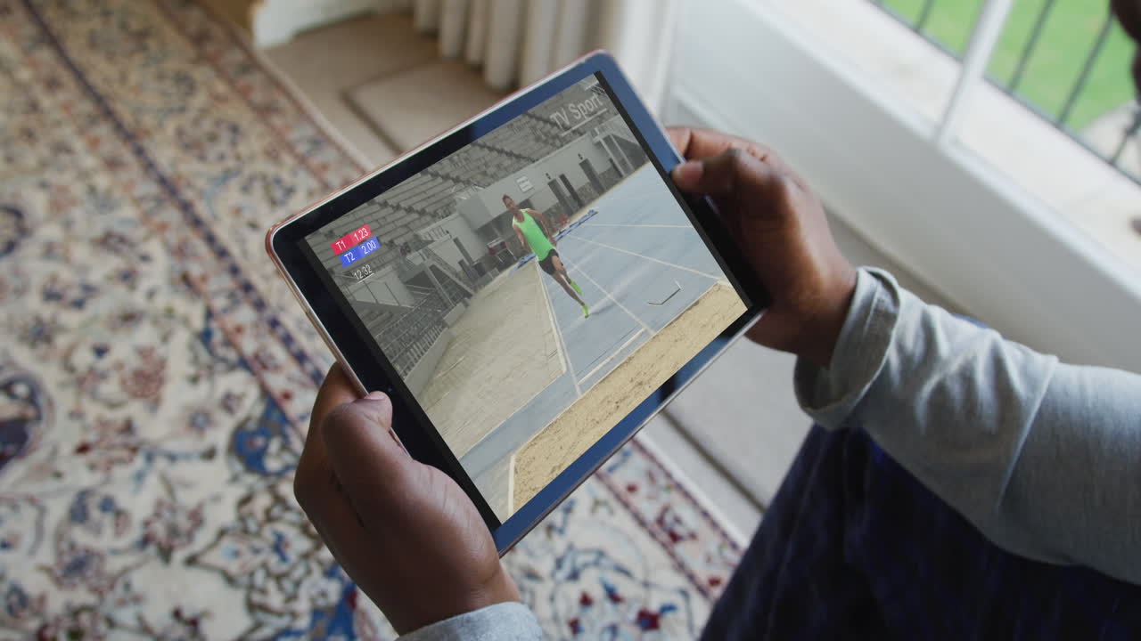 compuesto de un hombre sentado en casa, viendo el evento de salto de longitud de atletismo en la tableta
