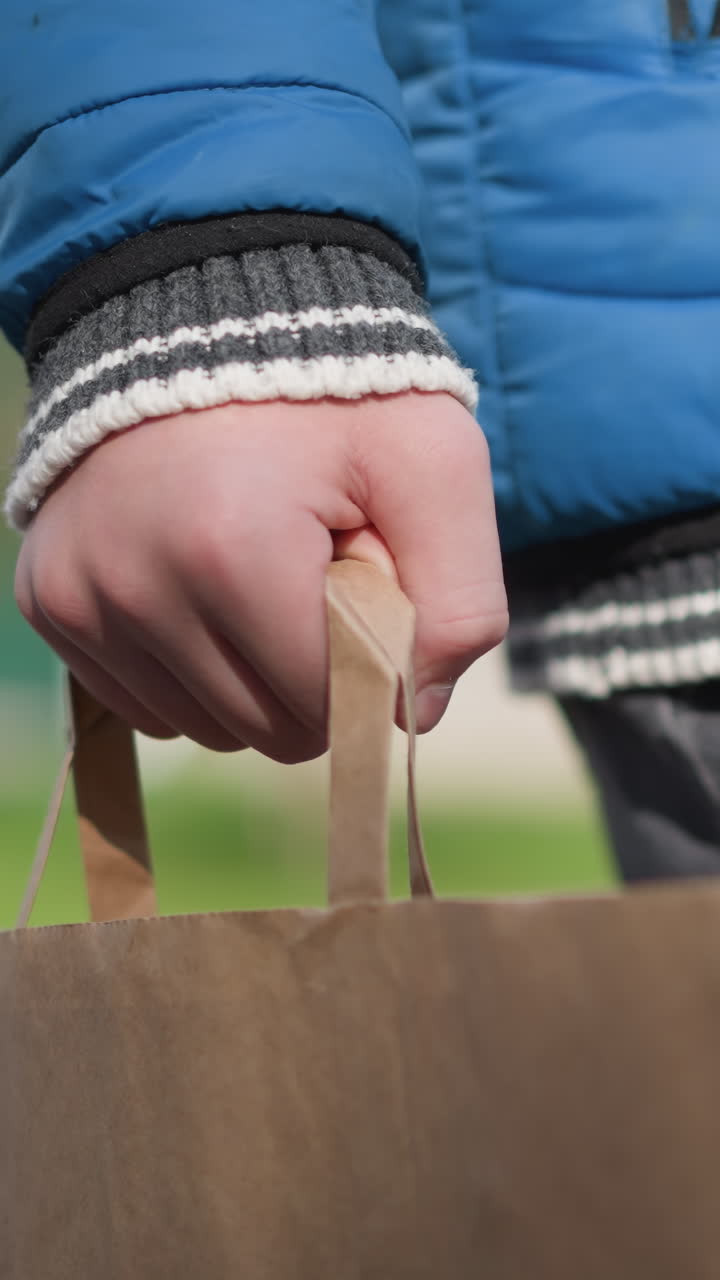 Close-up of a young boy's hand holding a paper bag while walking in a residential area shadows reflect on him, with vibrant autumn trees and a blurred background