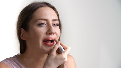 studio shot of attractive woman putting on lipstick