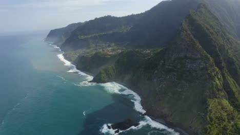 beautiful turquoise water comes in at the coast of madeira and crashing against the steep cliff of the mountain