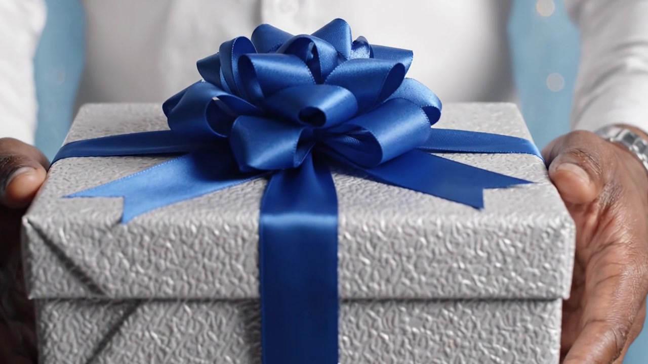 A beautifully wrapped gift box adorned with a striking blue ribbon, held carefully in hands, symbolizing celebration and joy in special moments.