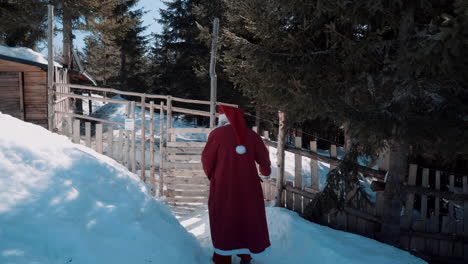 Santa-walks-along-a-snowy-path-to-a-wooden-house-with-a-wooden-fence