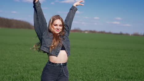 sexy model posing on camera outdoors. portrait of a beautiful young woman with long hair in short top and denim suit on green field in sunny day. slow motion.