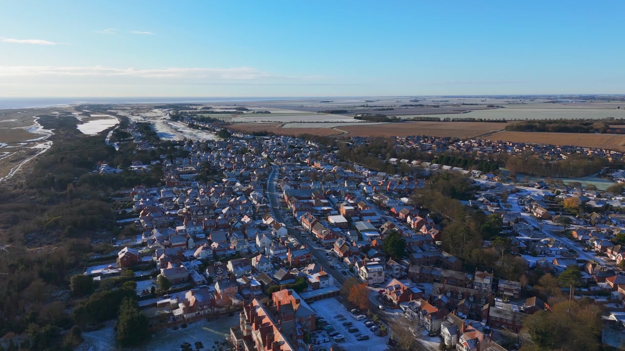 Sneeuw bedekt daken van de stad in een heldere luchtfoto. Roodpannendaken steken af tegen de witte sneeuw. Een rivier slingert door het landschap, omzoomd door open velden.