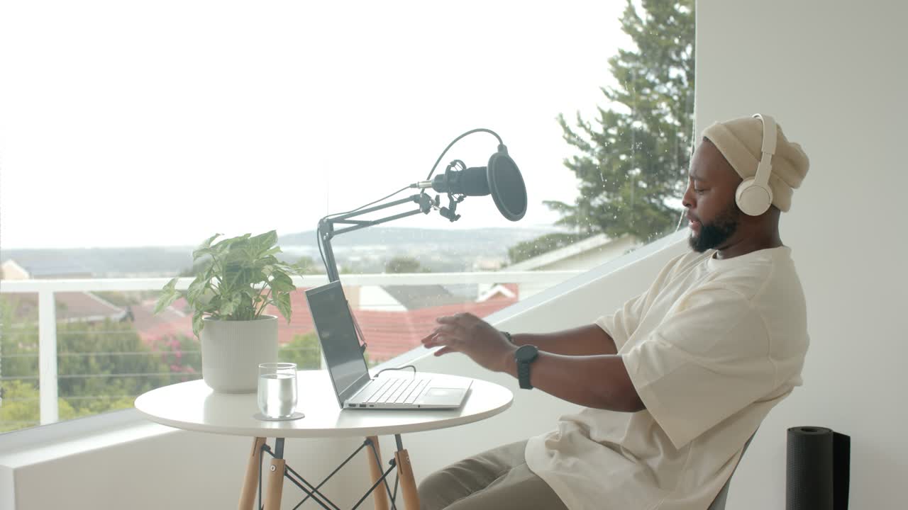 African American man in beanie hosting gesturing typing leaning on deck with laptop mic, copy space