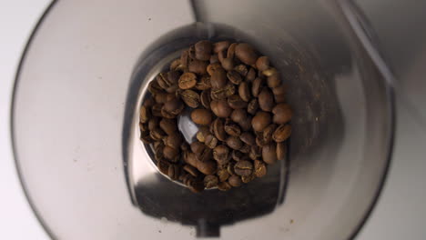 vista aérea de cerca de granos de café frescos y marrones que se vierten en un elegante molinillo eléctrico para el café de la mañana