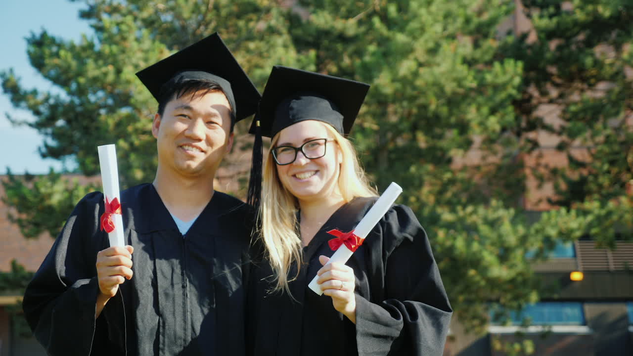 un retrato de dos graduados: un hombre asiático y una mujer caucásica con la ropa y las gorras del graduado