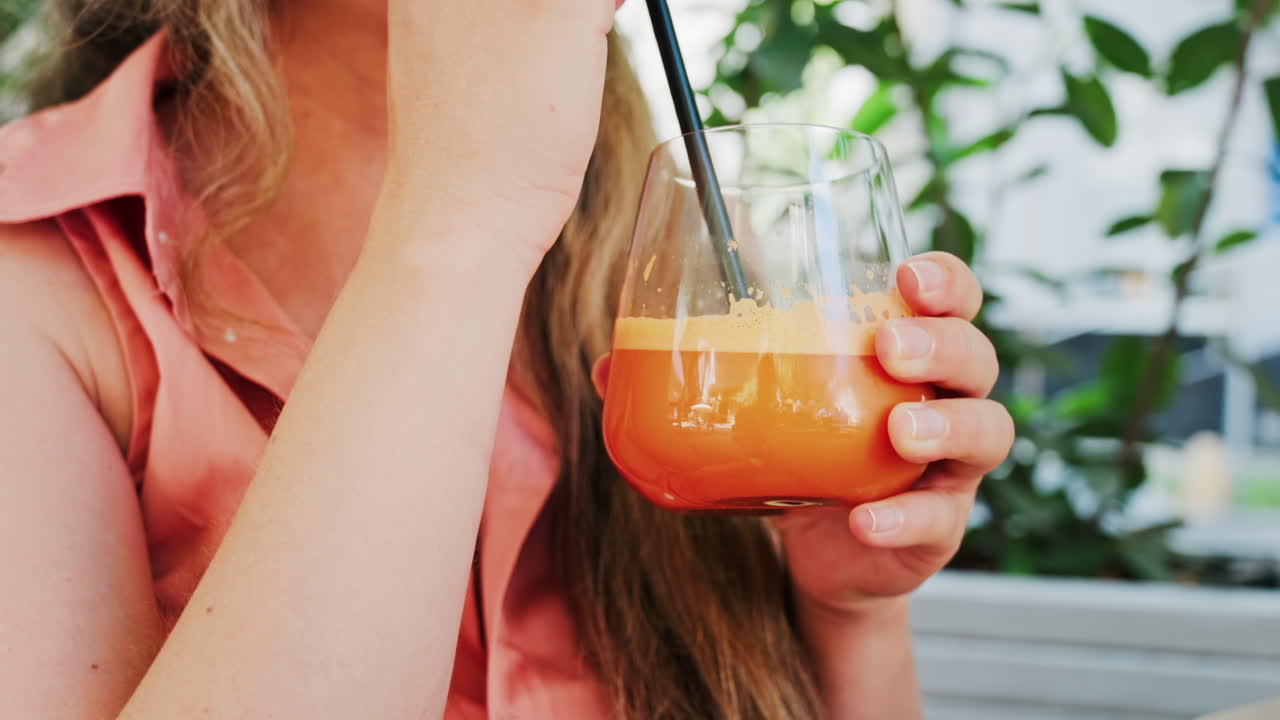 Close up of a woman drinking a glass of orange juice with a black straw