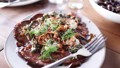 a beautifully plated filet mignon carpaccio garnished with fresh herbs and vegetables, captured in a well-lit, upscale dining environment