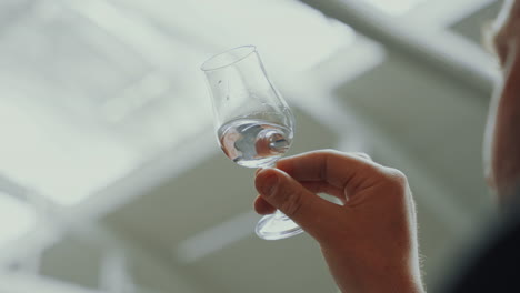 male analyst holding a glass with distilled gin while checking it, industrial process in a gin distillery production