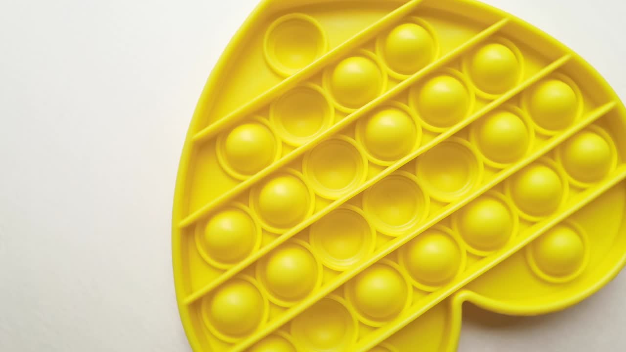 nuevo juguete para bebés. pop it juego de dedos. color gracioso. mano adulta apretando silicona redonda. cambio de forma. forma de corazón amarillo