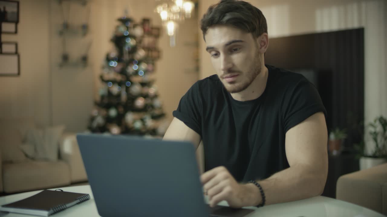 Happy man working on laptop computer at christmas. Smiling guy looking computer