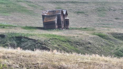 low level drone shot of an abandoned prairie homestead on the side of a grassy hill