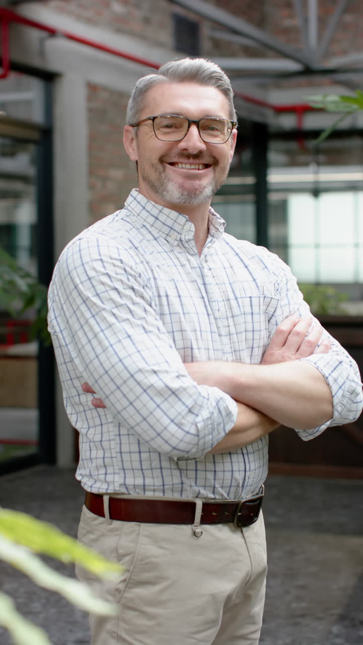 Vertical video of caucasian businessman with arms crossed smiling at office