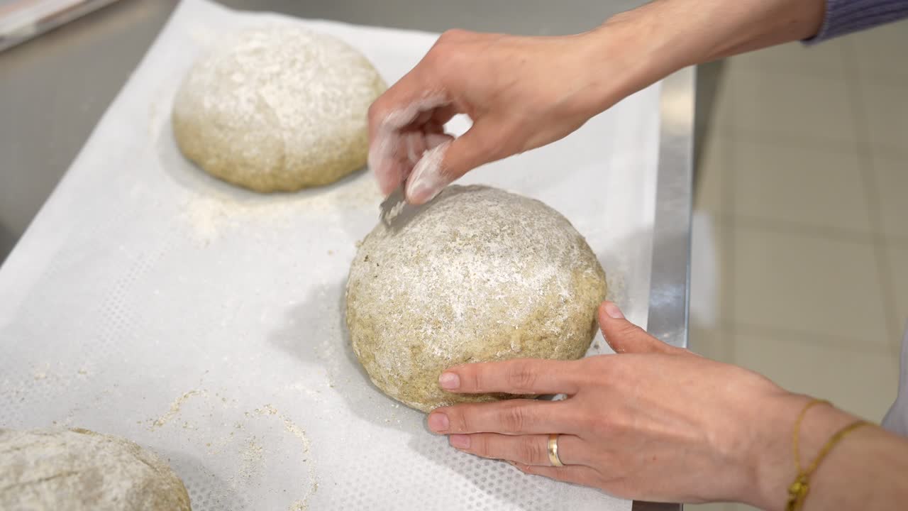 Baker's Hands Scoring Raw Bread Dough with a Lame