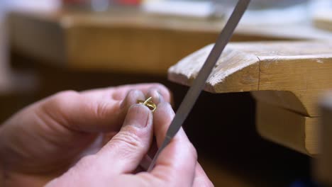 male jewelry maker hand filing a piece of jewellery in a workshop