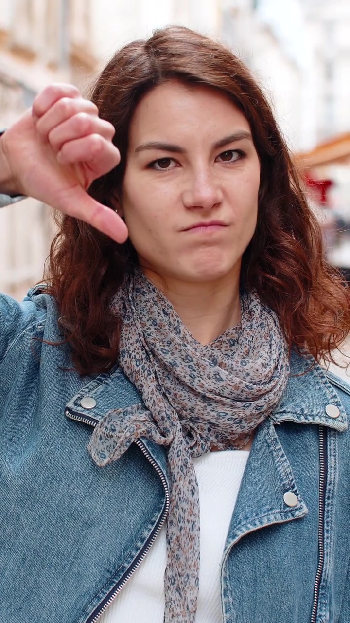 Giovane donna che fa un gesto di disapprovazione, camminando per una strada cittadina con aria contrariata durante un'uscita urbana all'aperto.