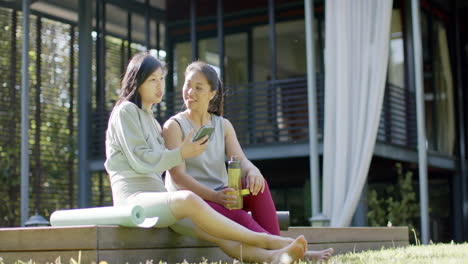 happy asian female friends with water bottle and smartphone smiling on terrace, slow motion