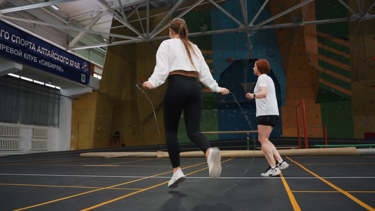 Dynamiczna praca nóg na korcie halowym pokazująca energiczne ćwiczenia badmintonowe ze sprintami, podskokami i zwinnymi obrotami, intensywny trening cardio i szybkie wymiany z partnerem, ścianka wspinaczkowa w tle i przestronne wnętrze