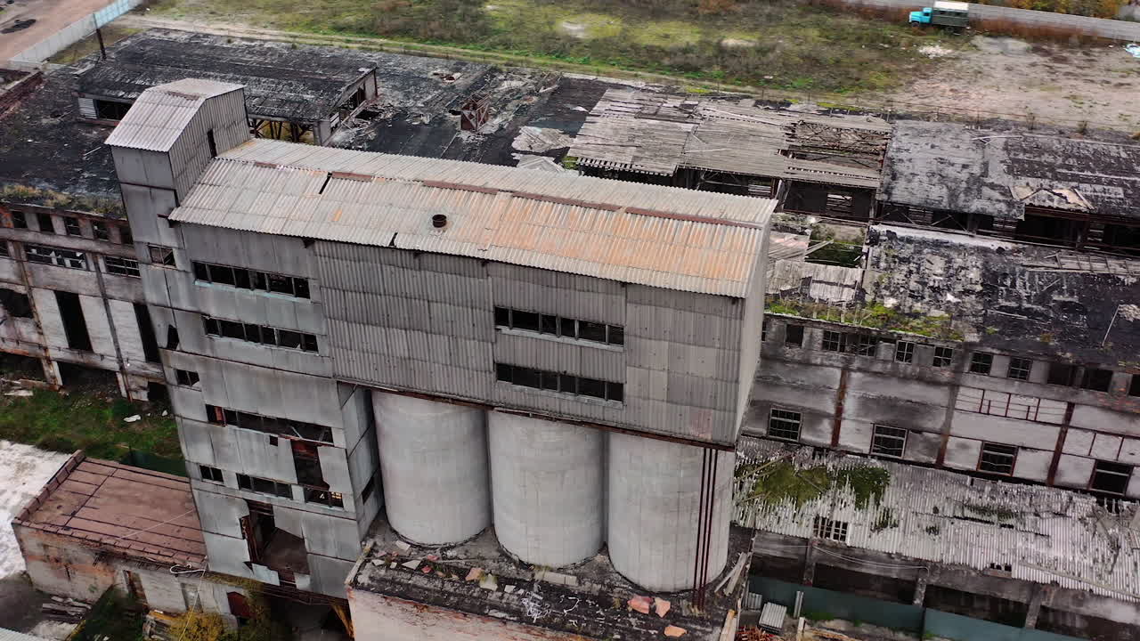Old abandoned plant. Damaged buildings on the field. Broken windows and roof of a ruined factory. Damaged industry. Aerial view.