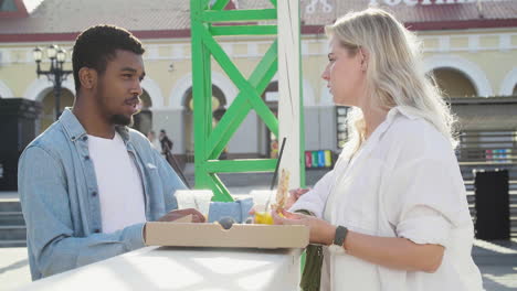 friends chatting while sharing pizza and drinking, standing at an outdoor table in the street 1