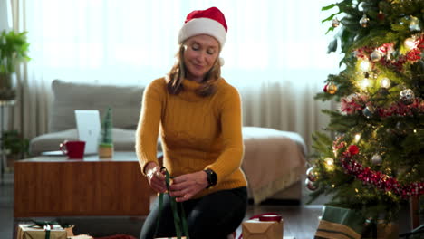 Smiling woman in Santa hat wrapping gifts by Christmas tree at home