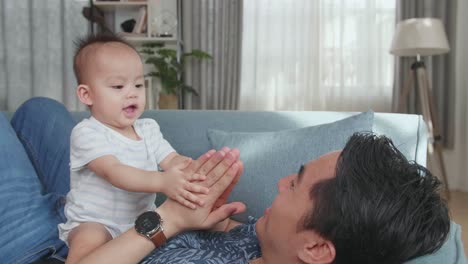 Asian Father And Son Playing On Sofa In Home