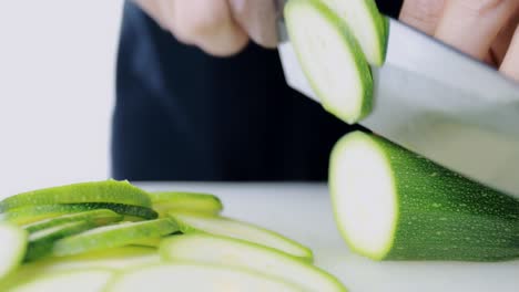4k women hand cutting fresh courgette on cutting board. female hand slices raw japanese cucumber into circles with knife on cutting board. healthy food concept.