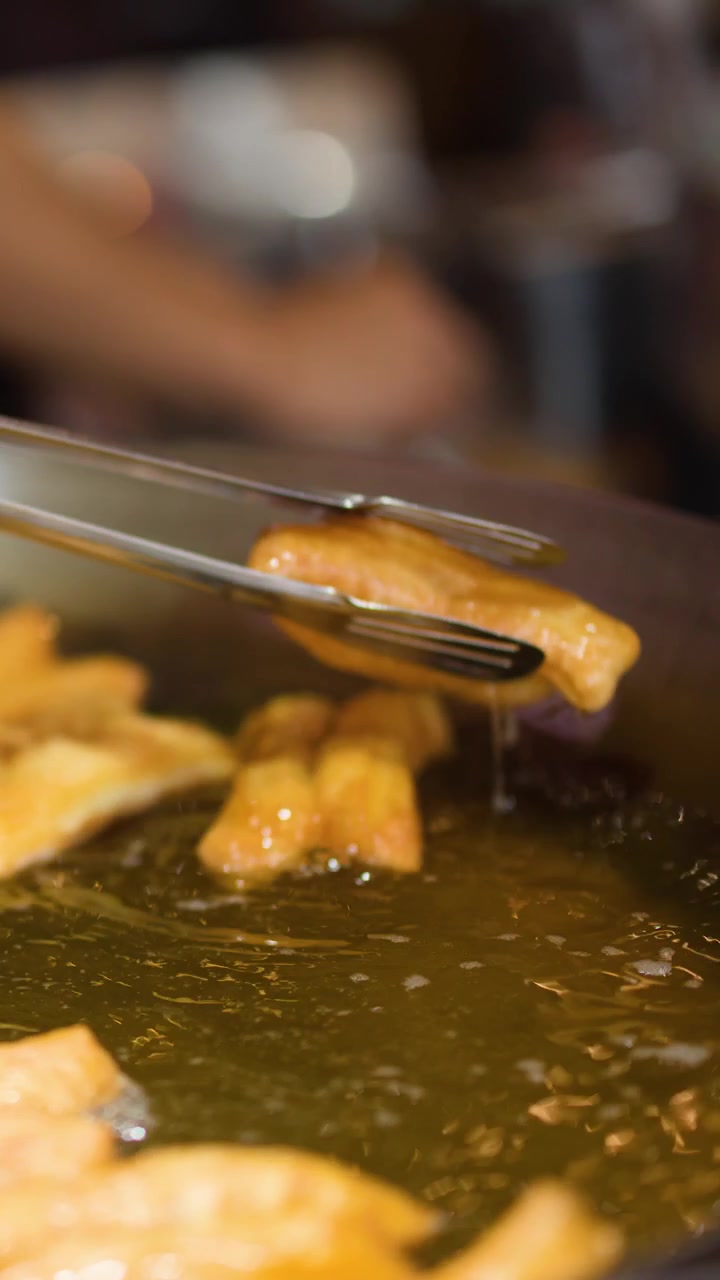 Close-up of hands using metal tongs to flip golden fried dough in bubbling oil.