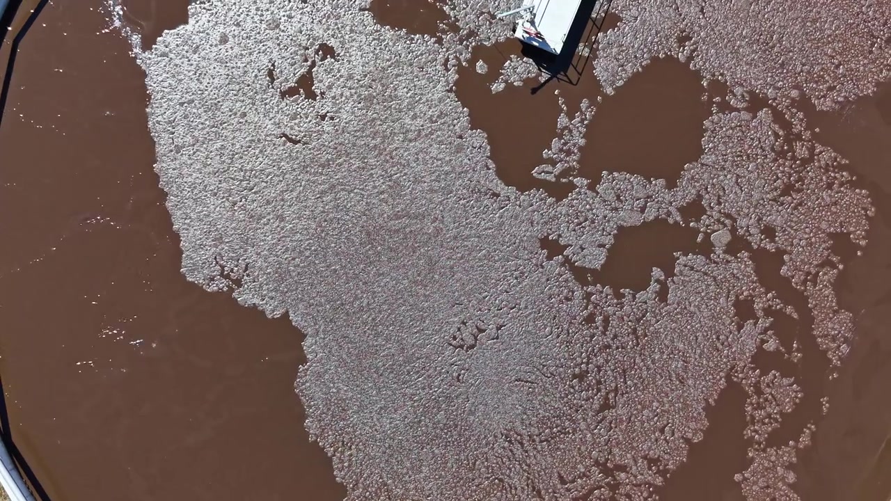 Acqua marrone scorre formando disegni vicino a strutture in una giornata di sole in un'area costiera, mettendo in mostra elementi naturali e artificiali a stretto contatto.