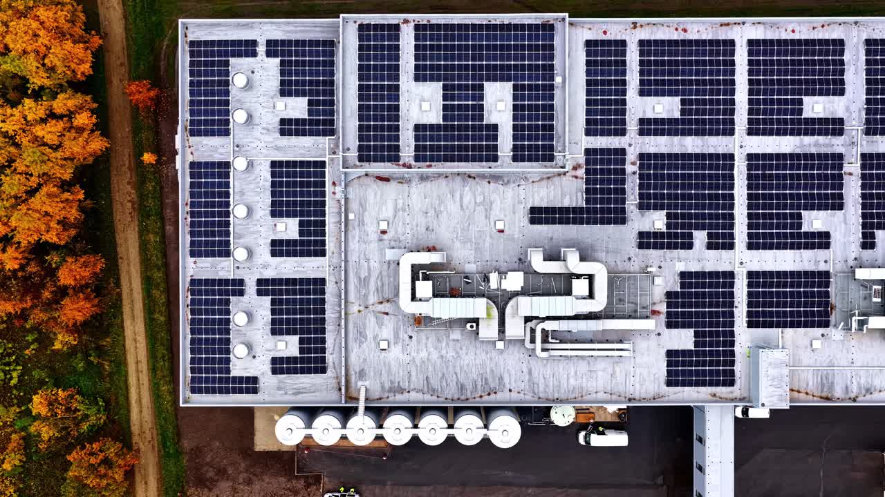 White modern building surrounded by colorful autumn trees from above, solar panels and industrial piping