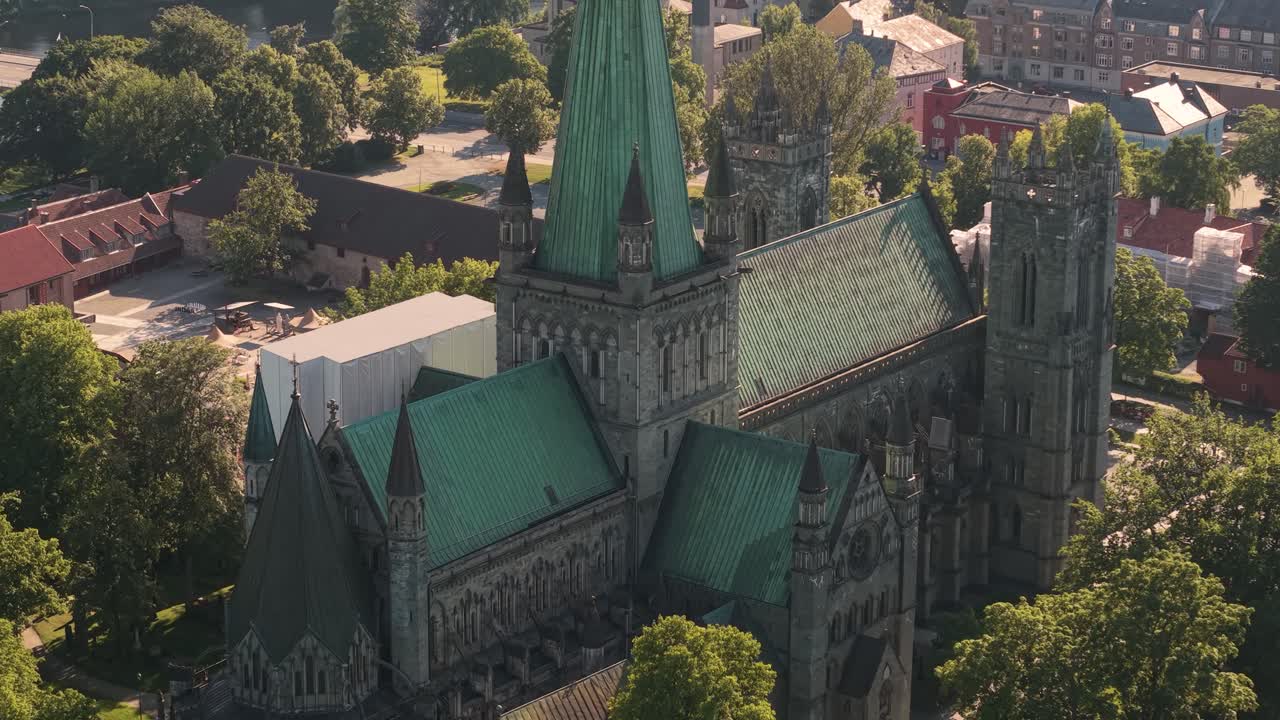 Os telhados verde-cobre e as torres góticas da Catedral de Nidaros se elevam acima das árvores ao redor em Trondheim, Noruega - Tomada orbital com drone