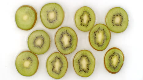 sur un fond blanc, des kiwis tranchés sont aspergés d'eau. l'eau tombe sur des kiwis juteux.