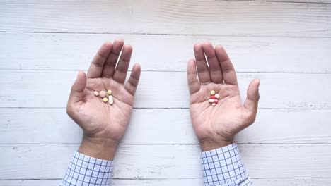 manos sosteniendo diferentes tipos de pastillas en una mesa de madera blanca