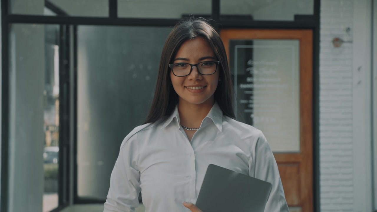 Jovem mulher profissional segurando um laptop fora de um escritório moderno