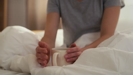 Close up of cup of coffee in woman&#039;s hand in the bed at morning