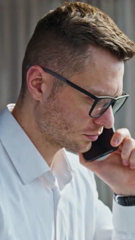 man in white shirt speaking on the phone looking worried. businessman concerned having phone conversation. vertical video