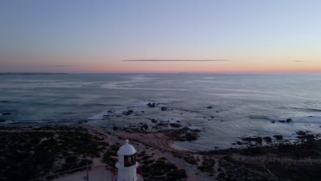 Corny-Point-lighthouse-reverse-aerial-reveal-in-evening-with-flashing-light-beacon,-Yorke-Peninsula,-South-Australia