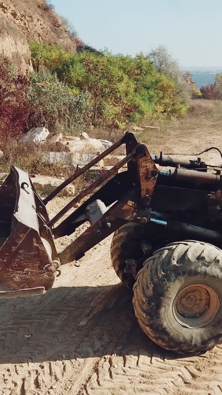 professional bulldozer with a bucket is picking up stones on sandy quarry against the backdrop of wild nature. Close-up. Vertical video