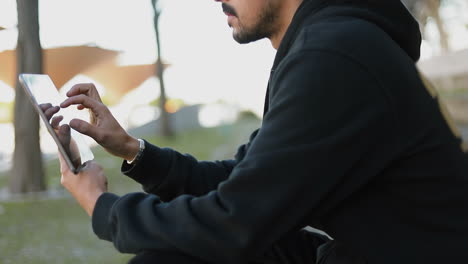 Medium-shot-of-young-Arabic-handsome-man-with-dark-curly-hair-and-beard-in-black-hoodie-sitting-on-stairs-outside