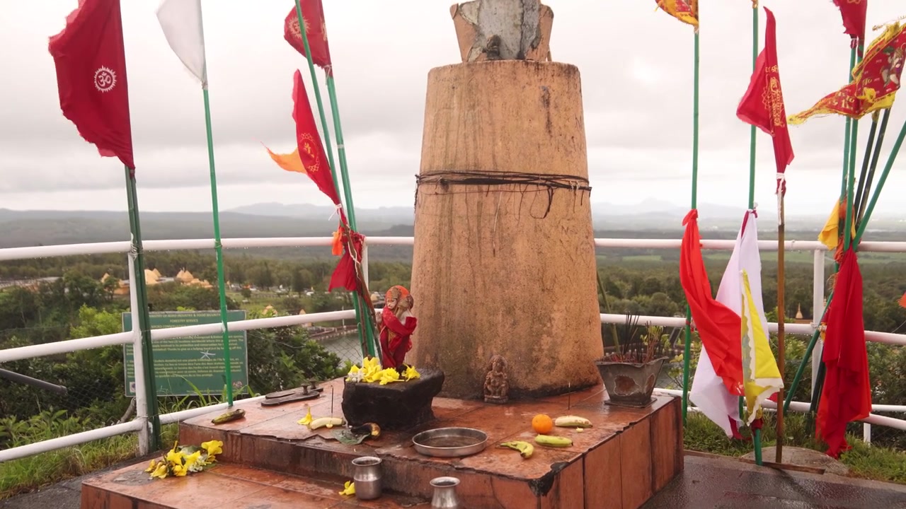 Mauritius'taki kutsal Ganga Talao tapınak kompleksinde dua bayrakları ve adaklarla süslenmiş Hindu sunağı. Tropikal manzaraya bakan Grand Bassin'deki yüksek tapınak.