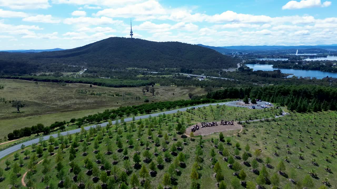 Drone aerial landscape of forest valley rolling hills town countryside lookout viewpoint with Black Mountain communications tower in Canberra ACT Australia tourism travel carpark Lake Burley Griffin
