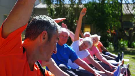 Side-view-of-Caucasian-male-trainer-training-senior-people-in-performing-exercise-at-the-garden-of-n