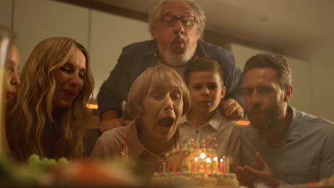 Familie-Gratuliert-Großmutter-Zum-Geburtstag.-Frau-Bläst-Kerzen-Auf-Kuchen