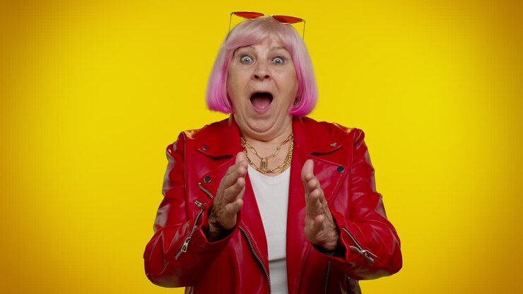 Anziana donna eccitata e stupita che alza le mani per la sorpresa guardando la telecamera, scioccata da una vittoria improvvisa