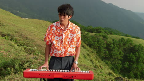 static shot of young man playing the piano surrounded by hilly terrain covered with lush green vegetation at daytime