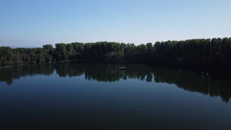 beautiful aerial footage of an european lake in the middle of the forest with reflecting trees and boat